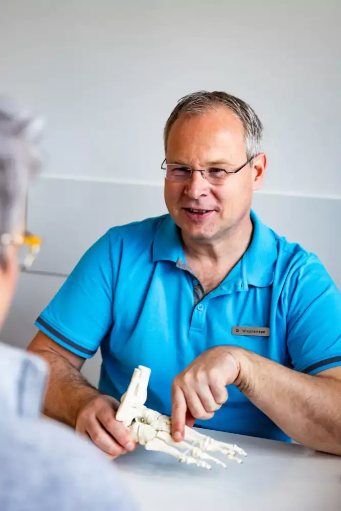 Arzt erklärt einer Patientin die Behanldungsschritte anhand eine Fußmodells
